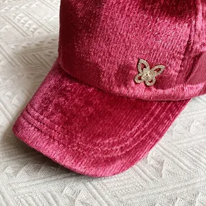 Dettaglio macro di un cappello da baseball in velluto magenta con una spilla a farfalla