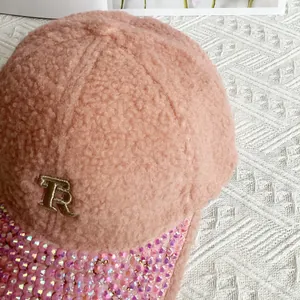 Detail of pink fleece baseball cap featuring rhinestone brim and golden metal R letter