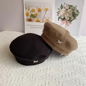 Detail of wool beret with butterfly metal charm in black and khaki colors