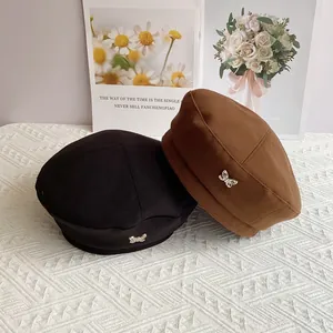 Detailed close-up of wool beret with small silver butterfly charm in black and brown