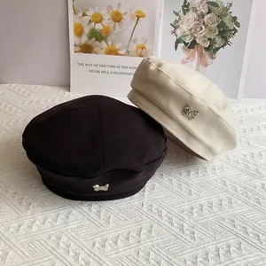 Detail of wool beret hats in black and cream featuring a silver metal butterfly buckle