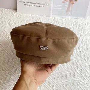 Close-up of brown wool newsboy cap featuring a detailed metal butterfly badge detail