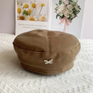 Detail of a brown wool beret featuring a silver metal butterfly ornament on a textured fabric
