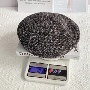 Détail d'un béret en tweed sur une balance montrant un poids de 103g pour la qualité