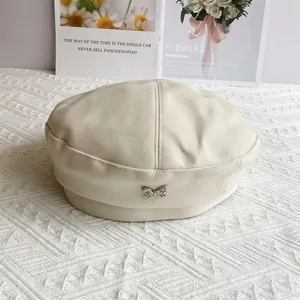 Close-up of cream wool beret featuring a detailed silver butterfly metal ornament