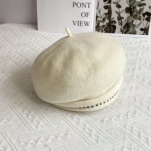 Close-up of cream wool beret with delicate metal stud trim and classic top stalk detail