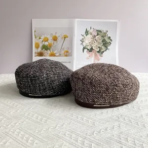 Détail de bérets en tweed gris et marron avec boucle métallique sur fond de tissu doux