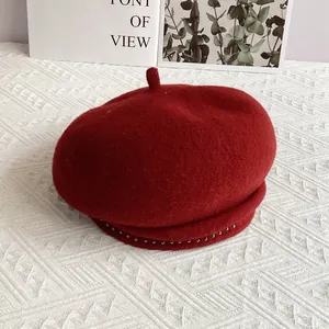 Close-up of wine red wool beret with silver bead trim and minimalist accent card