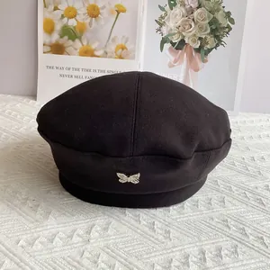 Detail shot of a black wool beret featuring a silver butterfly metal accessory decoration