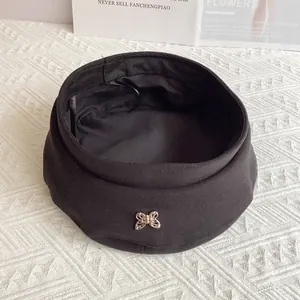 Detail of a black wool beret with a decorative golden butterfly metal buckle charm