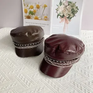 Brown and burgundy PU leather newsboy caps with metallic chain decoration on white cloth