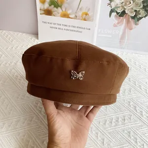 Detail view of brown wool beret featuring a metallic butterfly emblem and warm texture