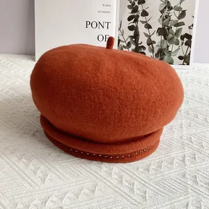 Detailed view of caramel wool beret with silver studs on textured white fabric