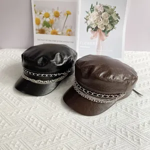 Close-up of black and brown PU leather newsboy hats with silver chain decor on a desk
