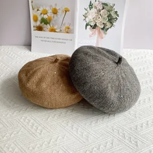 Detail of chenille knit berets in grey and camel with subtle sequins on a textured mat