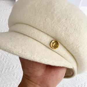 Détail du béret crème montrant la texture de laine fine et le bouton en métal doré