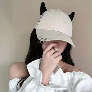 Dettaglio cappello beige con corna nere, anelli di metallo e dettagli a croce in stile