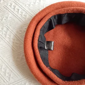 Detail view of the orange wool beret interior showing the quality label and size tag