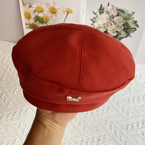 Detail of dark red wool beret featuring a vintage metal butterfly ornament decoration