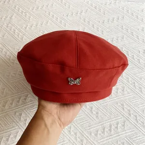Close-up of a red wool beret featuring a delicate silver butterfly metal ornament