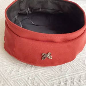 Detailed view of orange beret showing metal butterfly ornament and adjustable inner lining