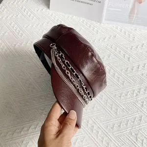 Close-up of wine red PU leather baker boy hat with silver chain detail on white table