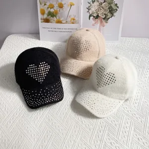 Angled view of three warm knit baseball caps with rhinestone hearts in black, beige, and white