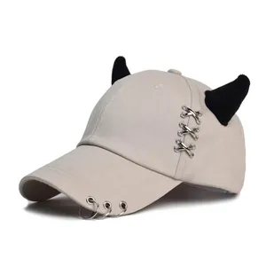 Dettaglio cappello beige con corna di diavolo nere, occhielli e anelli in metallo