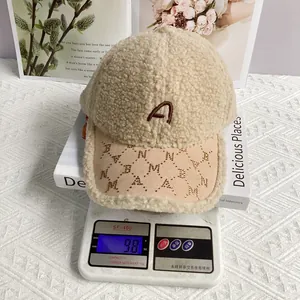 Nahaufnahme der beige Fleece-Kappe mit 'A'-Stickerei und 98g Gewicht auf Waage