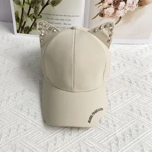 Detail of beige baseball cap featuring punk rivets on cat ears and side text logo