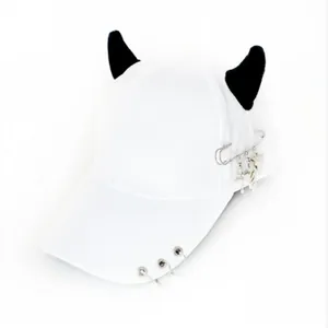 Dettaglio di un cappello da baseball bianco con corna da diavolo nere e anelli metallici