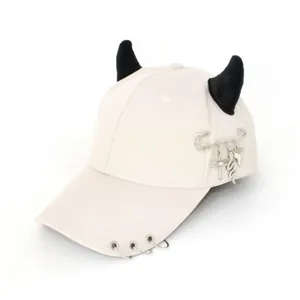 Dettaglio cappello baseball beige con corna da diavolo, anelli metallici e pendenti punk