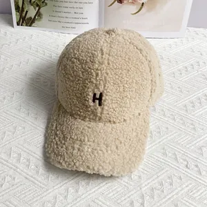 Close-up of beige faux lamb wool texture and brown letter H embroidery on baseball cap