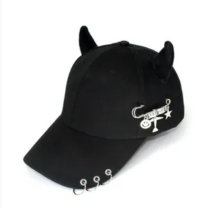 Dettaglio del cappellino nero con corna di diavolo, anelli metallici e ciondoli a spilla