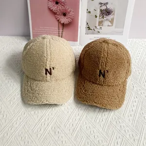 Close-up of N' embroidery on plush lamb wool baseball caps in beige and coffee colors