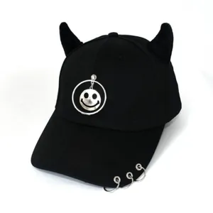 Dettaglio cappello da baseball nero in cotone con corna, ciondolo smiley e anelli visiera
