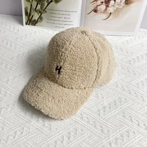 Close-up of beige sherpa baseball cap with brown embroidered H logo and soft texture