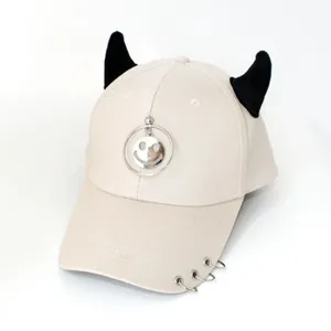 Dettaglio del cappellino beige con corna da diavolo nere e ciondolo smile in metallo