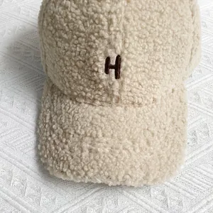 Close-up of the plush beige fleece fabric and embroidered letter H on the baseball cap