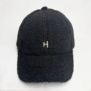 Close-up of black fuzzy sherpa baseball cap featuring beige embroidered letter H detail
