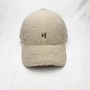 Detailed close-up of the beige sherpa baseball cap featuring a brown embroidered H letter