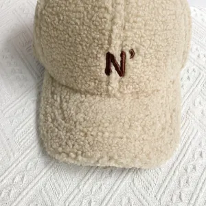 Macro shot of beige lamb wool baseball cap featuring brown embroidered letter N detail