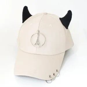 Dettaglio del cappellino beige con corna da diavolo nere e ciondolo della Torre Eiffel
