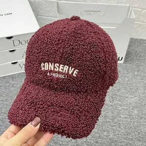 Detailed close-up of burgundy teddy fleece baseball cap with cream letter embroidery