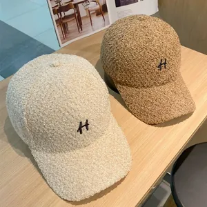 Teddy fleece baseballcaps met H-borduurwerk in beige en camel op houten tafel