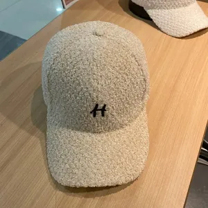Detailopname van de beige teddy fleece stof en het zwarte H-borduurwerk op de pet