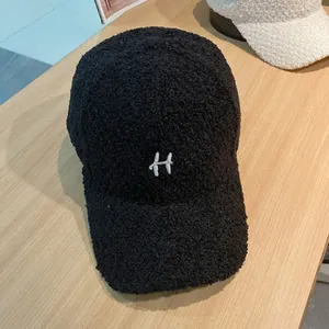 Detail van geborduurde witte letter H op zwarte teddy fleece winter honkbalpet