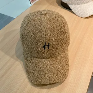 Detail van de bruine teddyfleece stof en zwart geborduurde letter H op de honkbalpet voor dames