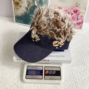 Close-up of blue denim sun visor cap with wig hair and leopard heart patch on weight scale