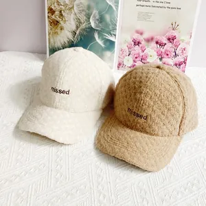 Detail der MISSED-Stickerei auf warmen Sherpa-Basecaps in Creme und Khaki-Farbe